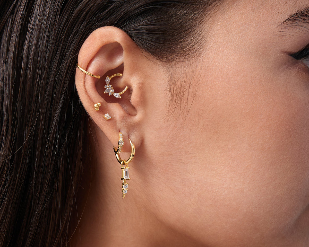 Close-up of a woman's ear wearing gold earrings with a blurred background